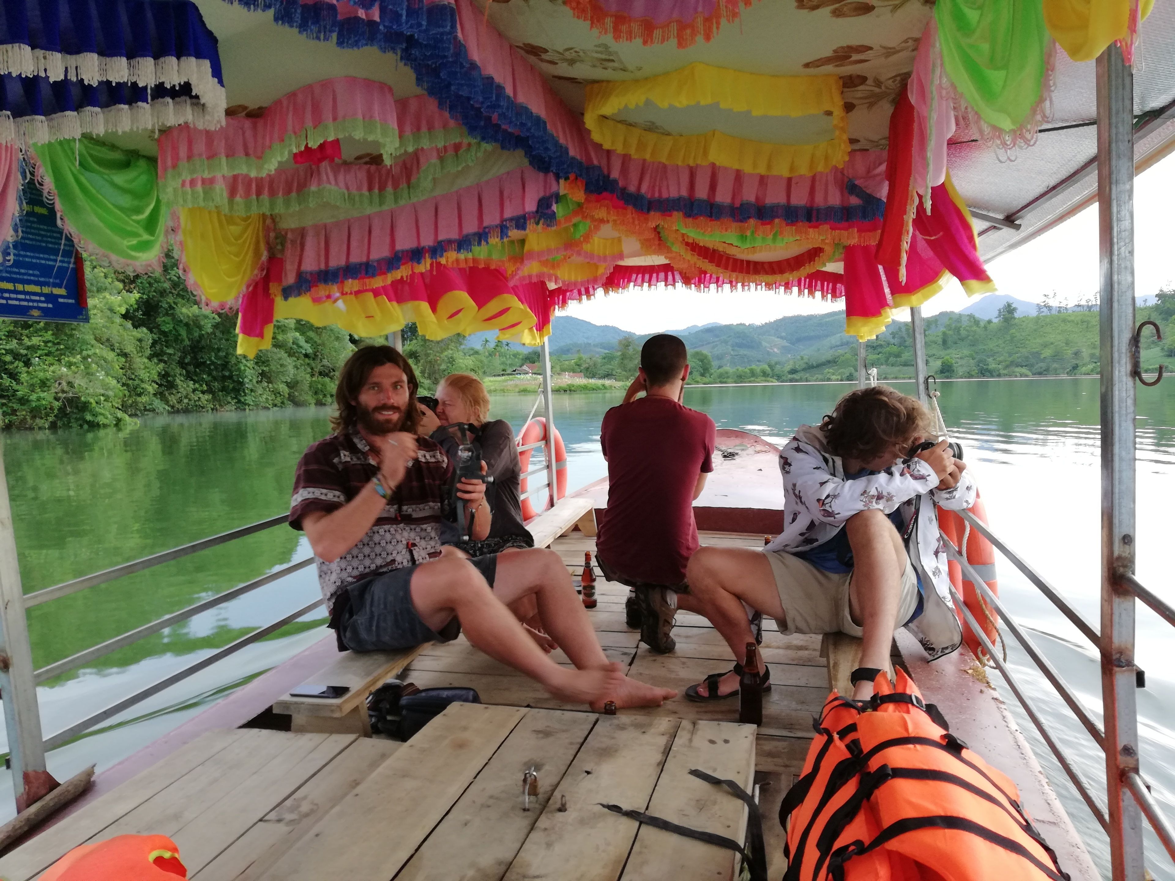 A boat with a wooden deck, passengers, and a river view.