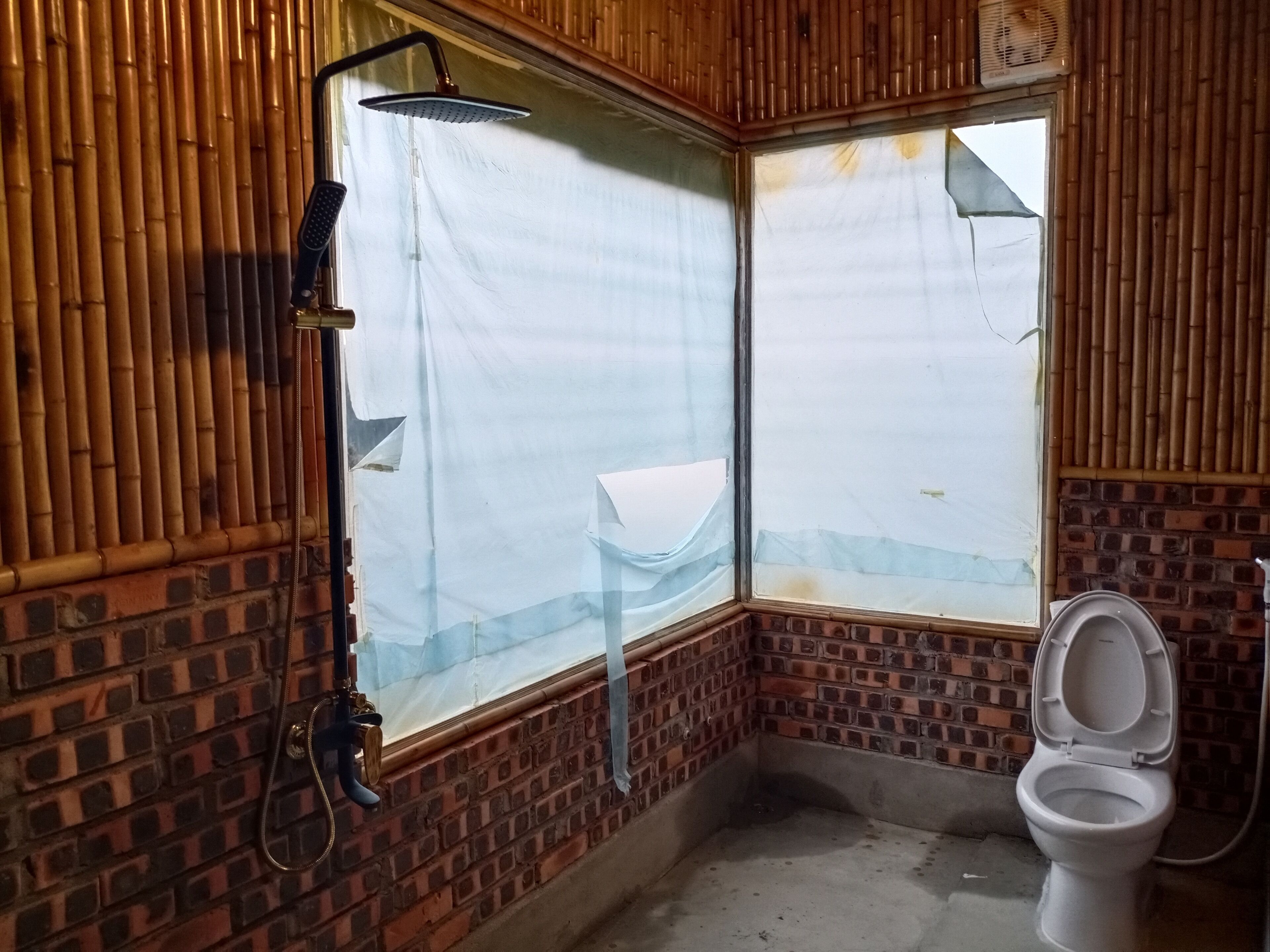 Casa de banho com chuveiro, sanita e janela com parede de bambu.