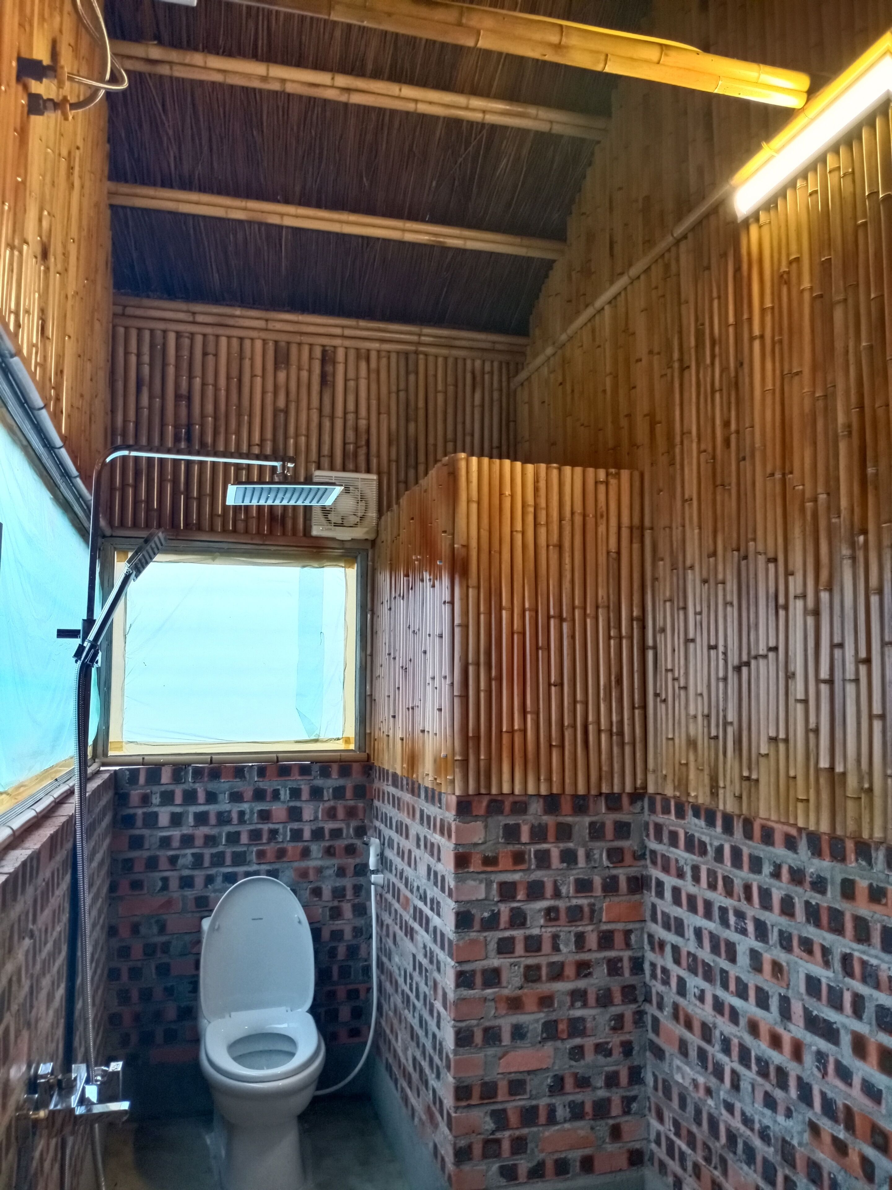 A bathroom with a bamboo wall, a window, and a toilet.