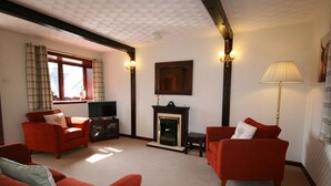 A living room with red sofas, a fireplace, and a television. - Highgarry Cottage (Invergarry)