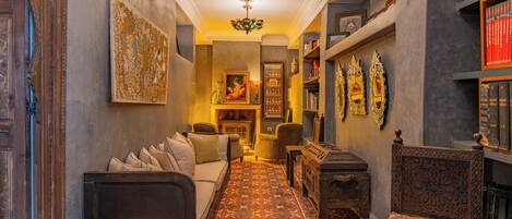 A narrow hallway with a patterned carpet, a sofa, a wooden cabinet, and a chair.