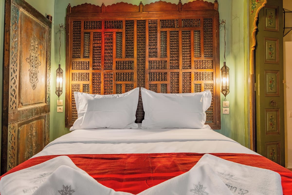 A bed with a white and red bedspread, a wooden headboard with intricate designs, and two wall-mounted lamps.