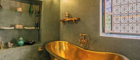 A vintage bathroom with a freestanding bathtub, shelves with toiletries, and a decorative window.