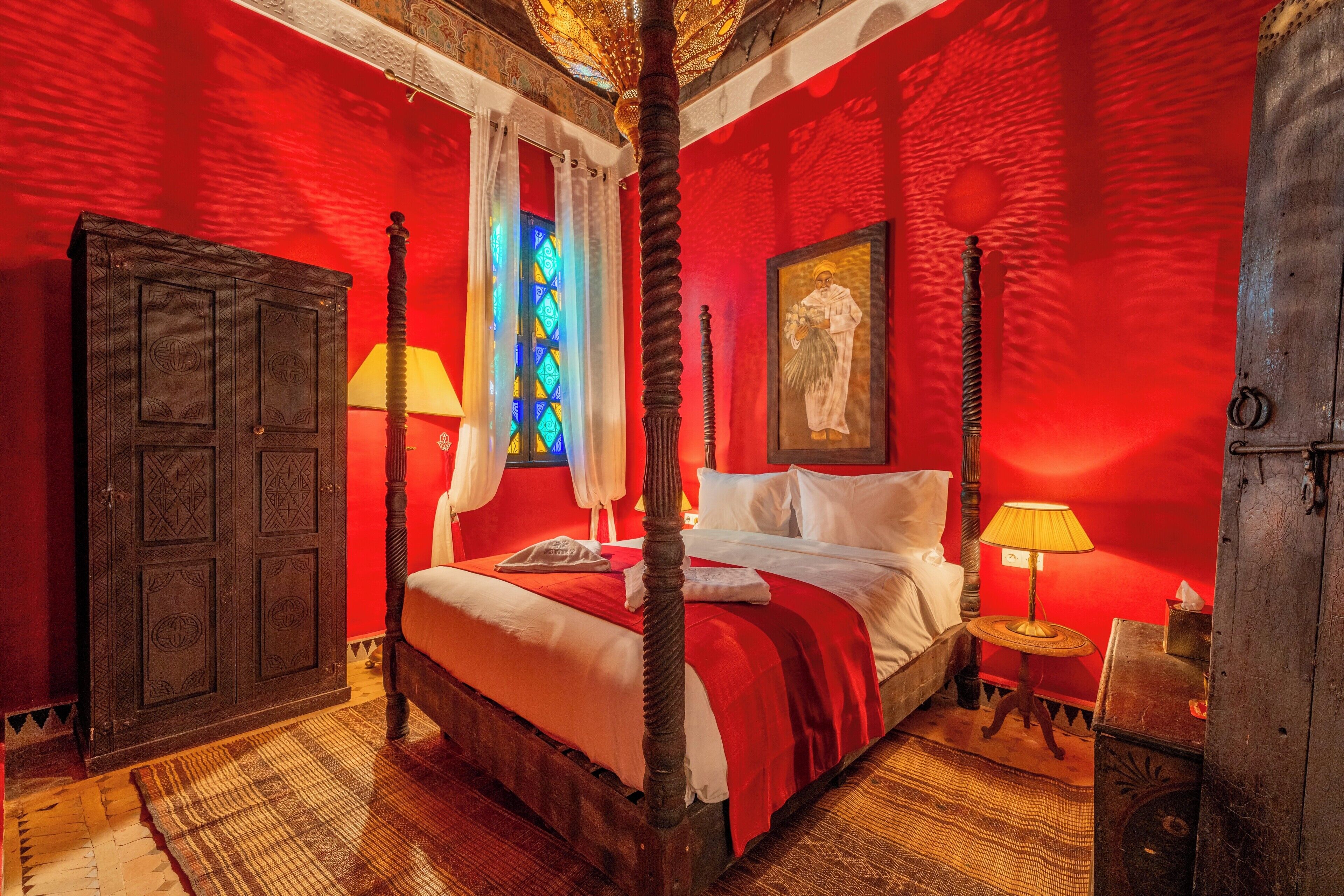 A room with a four-poster bed, a large stained glass window, and a wooden wardrobe.
