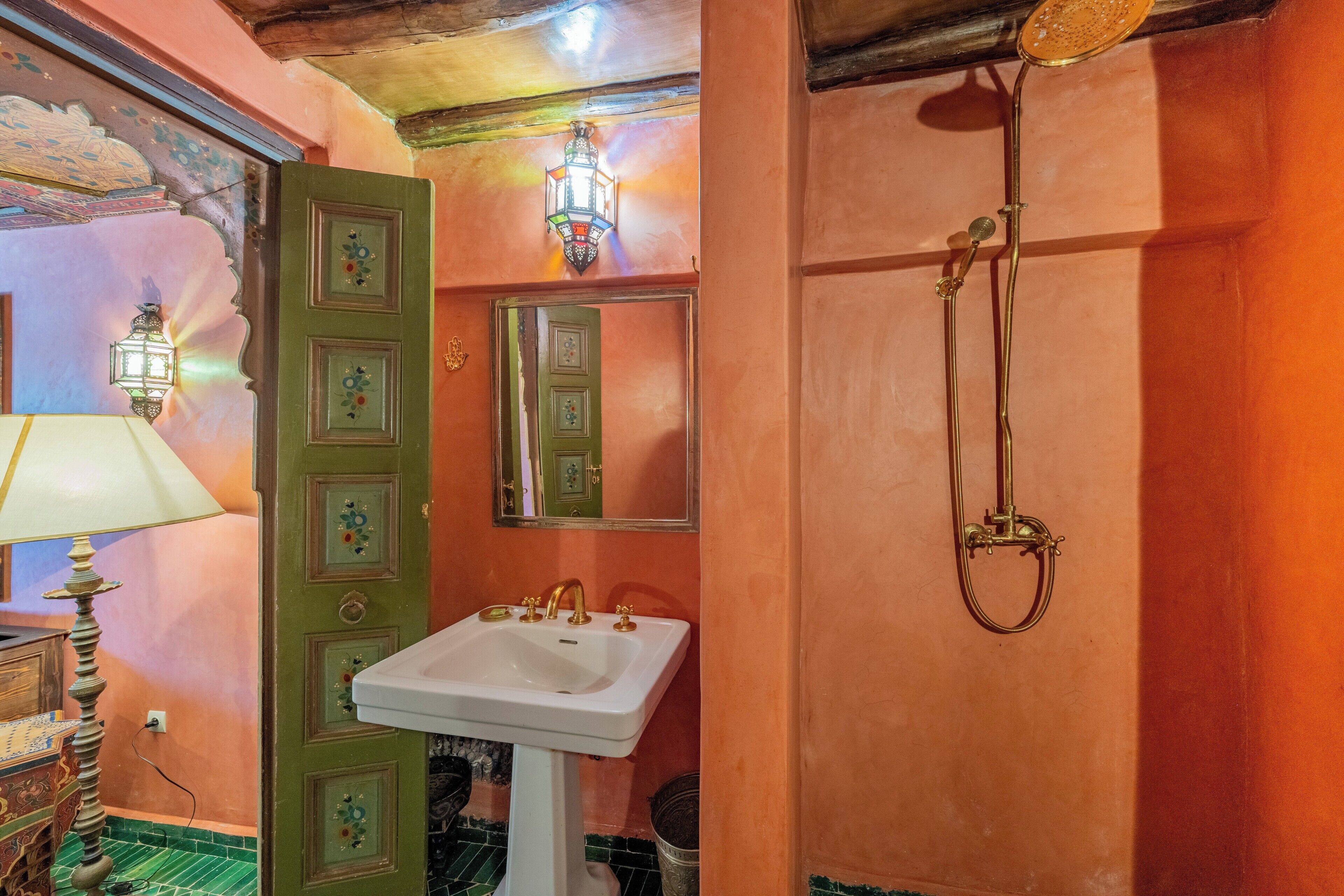 Une salle de bain avec une porte verte, un lavabo blanc, un miroir et une douche dotée d’un pommeau doré.