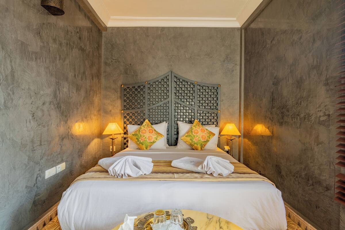 A neatly made bed with white linens, two decorative pillows, and a headboard with a geometric pattern.