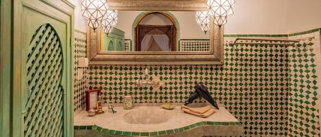 A bathroom with a green door, a sink with a mirror above, and patterned tiles on the walls.