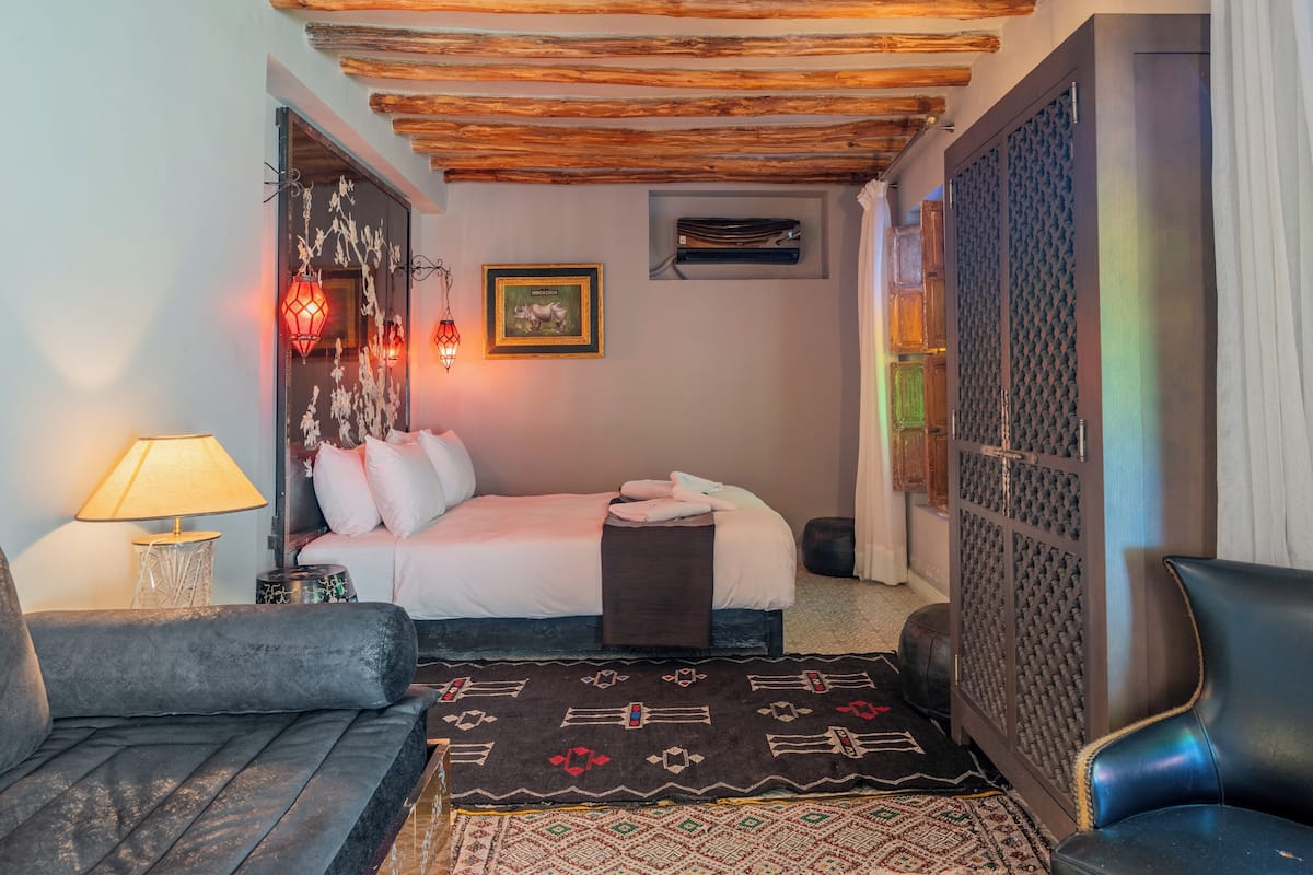 A cozy room with a bed, a sofa, a patterned rug, and a decorative wall piece.