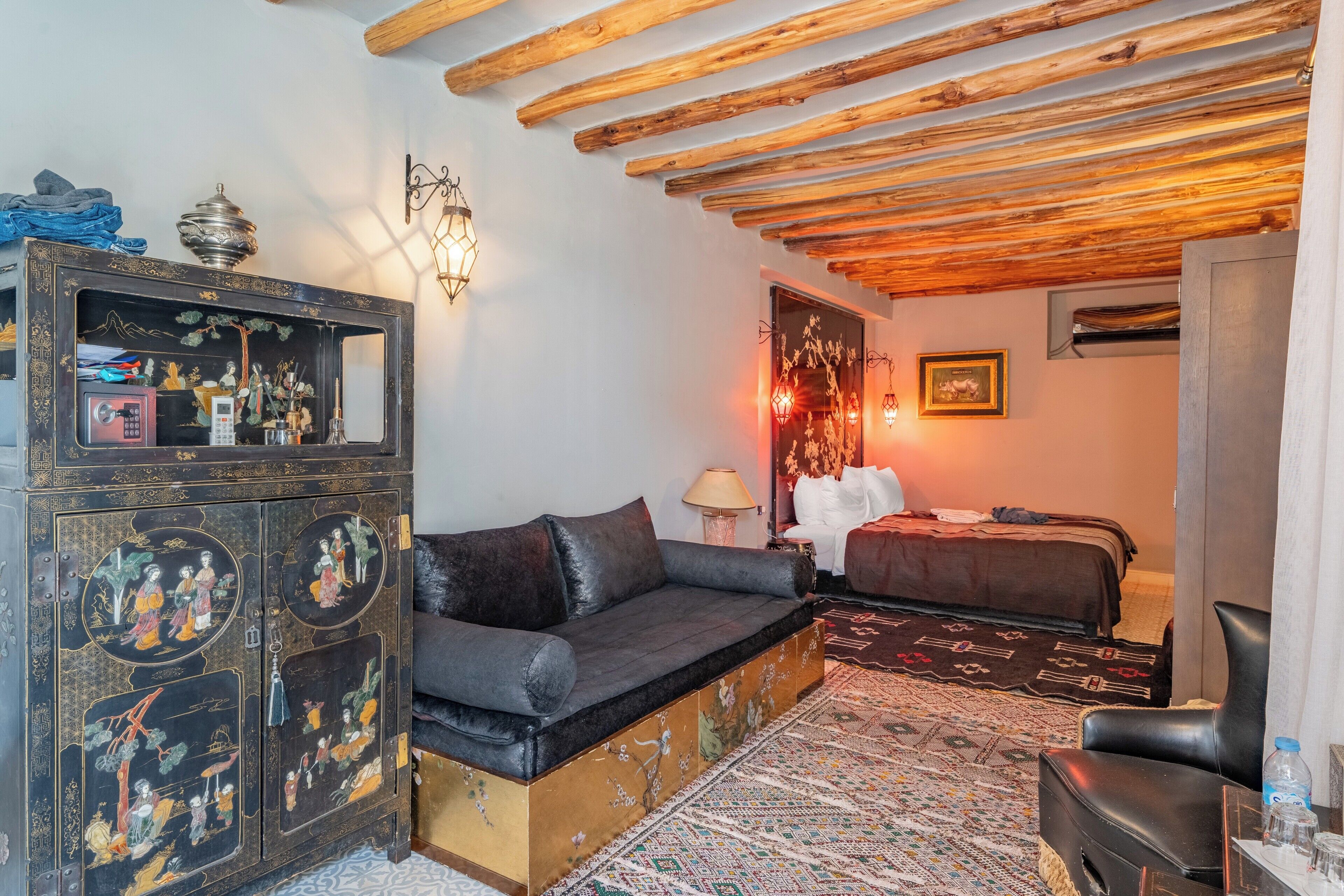 Una habitación con sofá, un armario con obras de arte, cama y alfombra estampada.