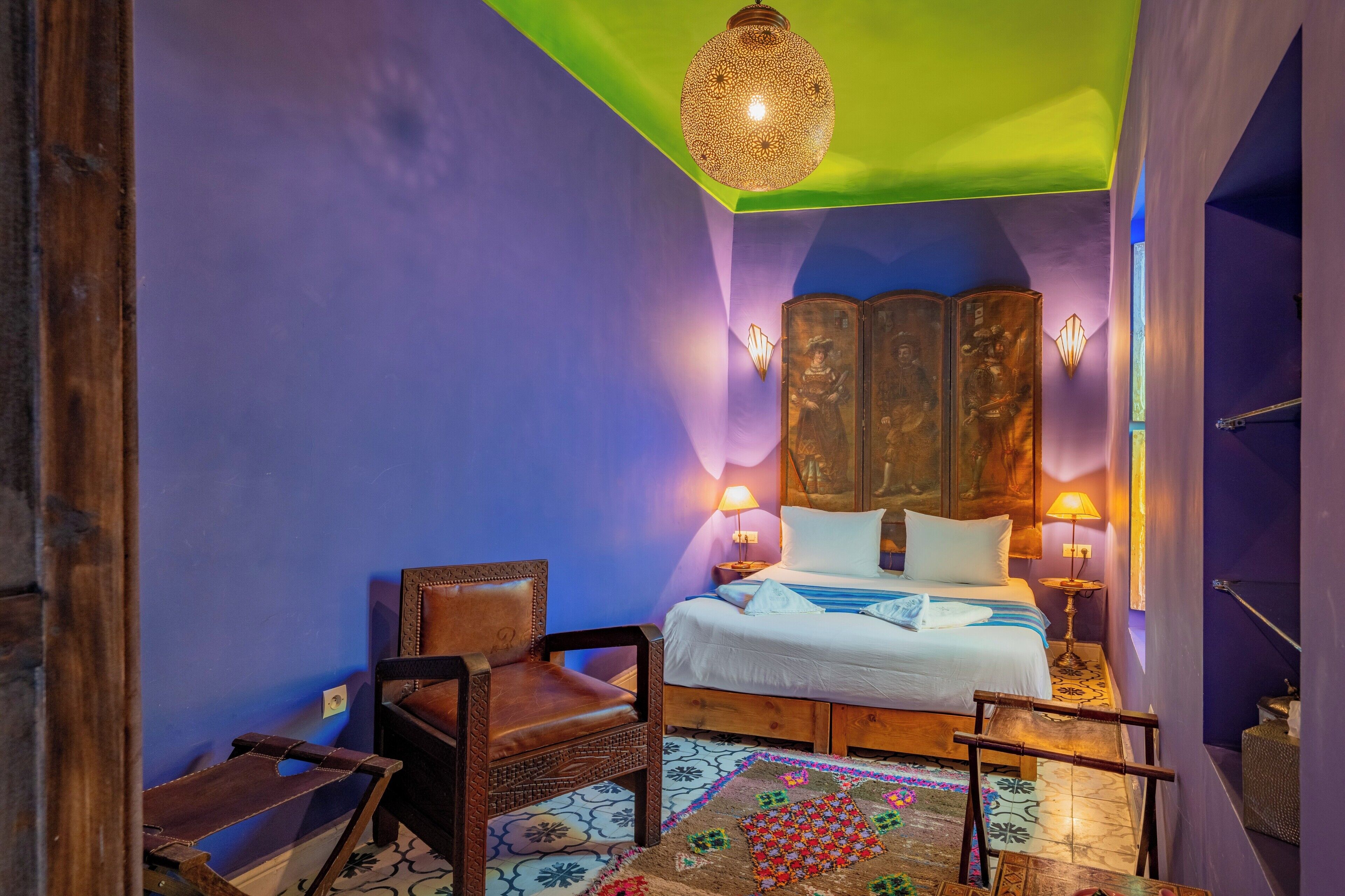 A room with a bed, two chairs, a wooden cabinet, and a hanging light fixture.
