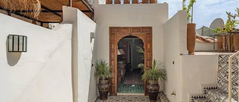 Un patio estrecho con baldosas decorativas, una puerta de madera y plantas en macetas.