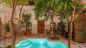 A pool area with tiled flooring, wooden furniture, and potted plants. - Riad Yamina52 (Marrakech)