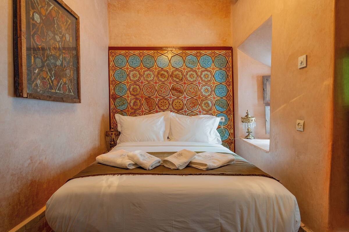 A hotel room with a large bed, a decorative headboard, a painting on the wall, and a window with a view.