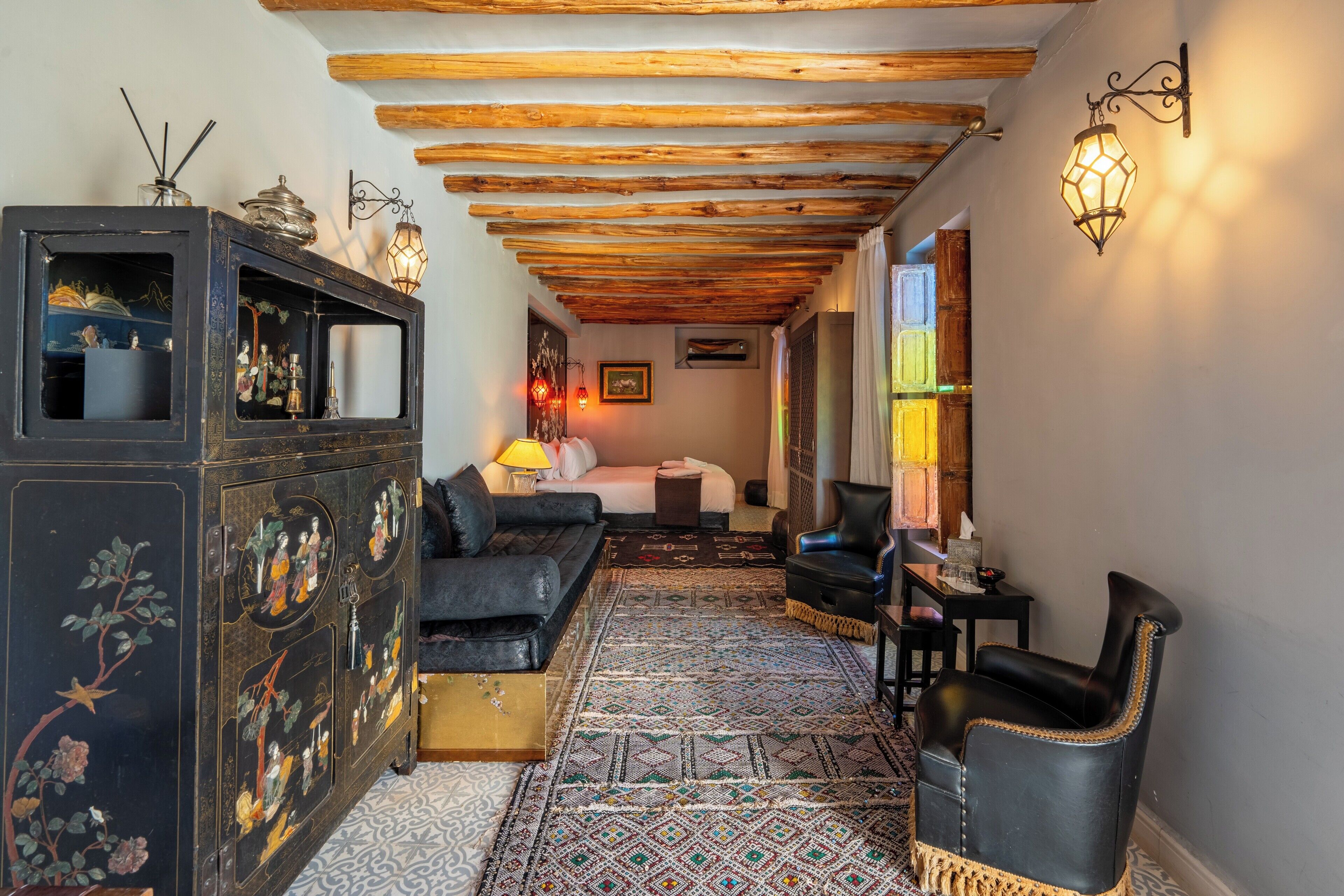 A hallway with a patterned rug, a sofa, a cabinet with decorative items, and a chair.