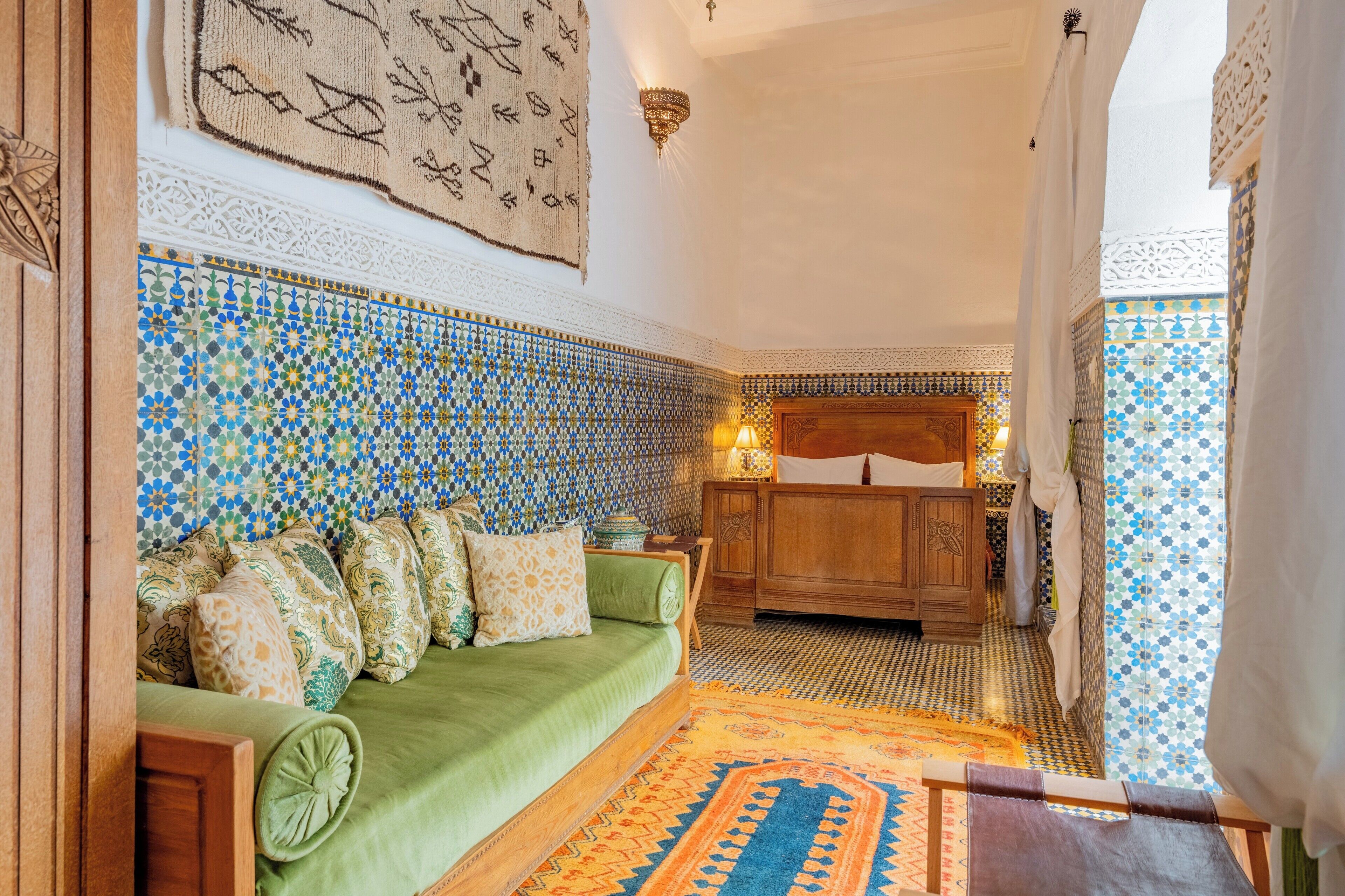 A traditional Moroccan room with a green sofa, patterned tiles, and a wooden cabinet.