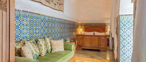 A traditional Moroccan room with a green sofa, patterned tiles, and a wooden cabinet.
