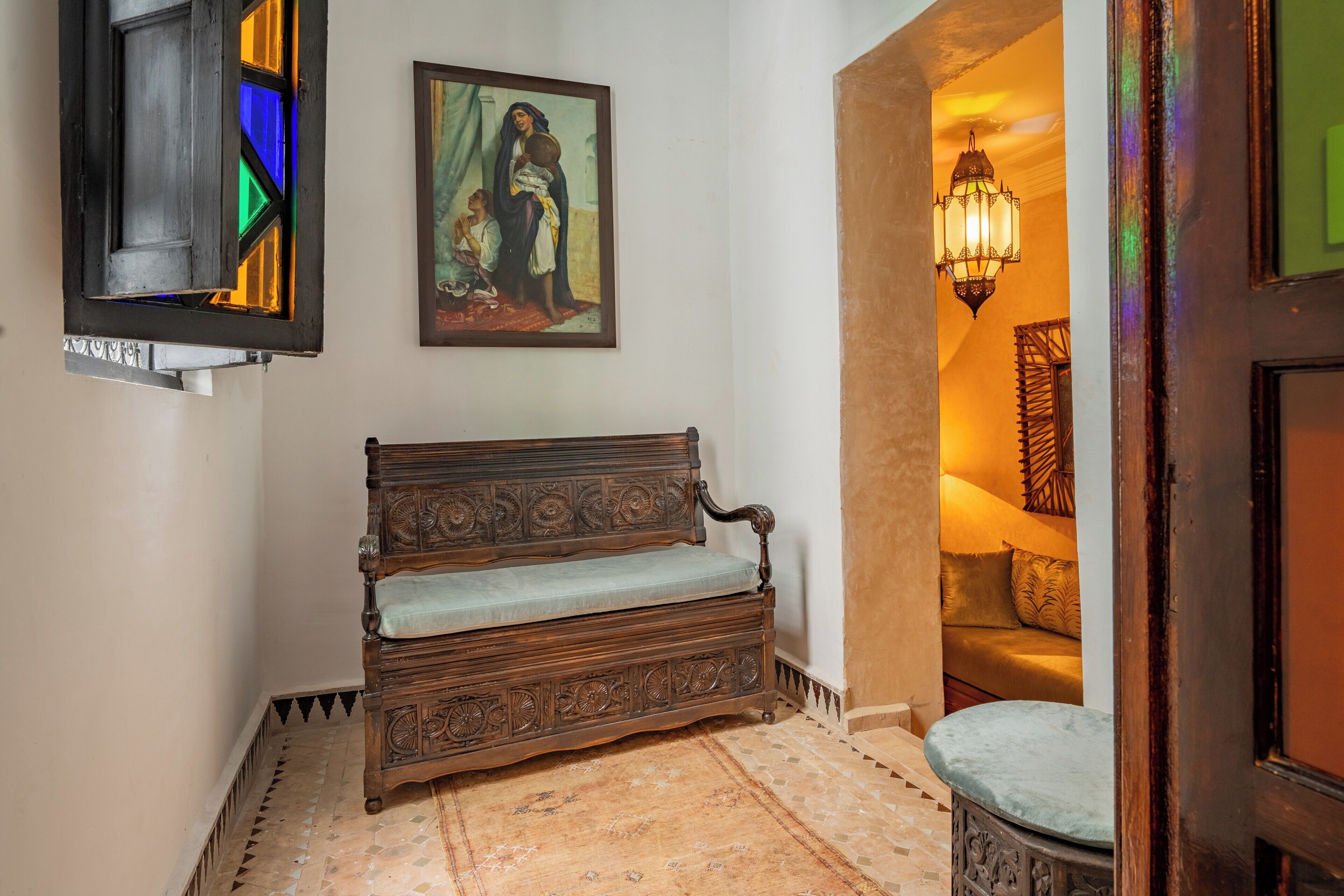 Un banco de madera con intrincados grabados, una ventana de vitral y un cuadro en la pared.