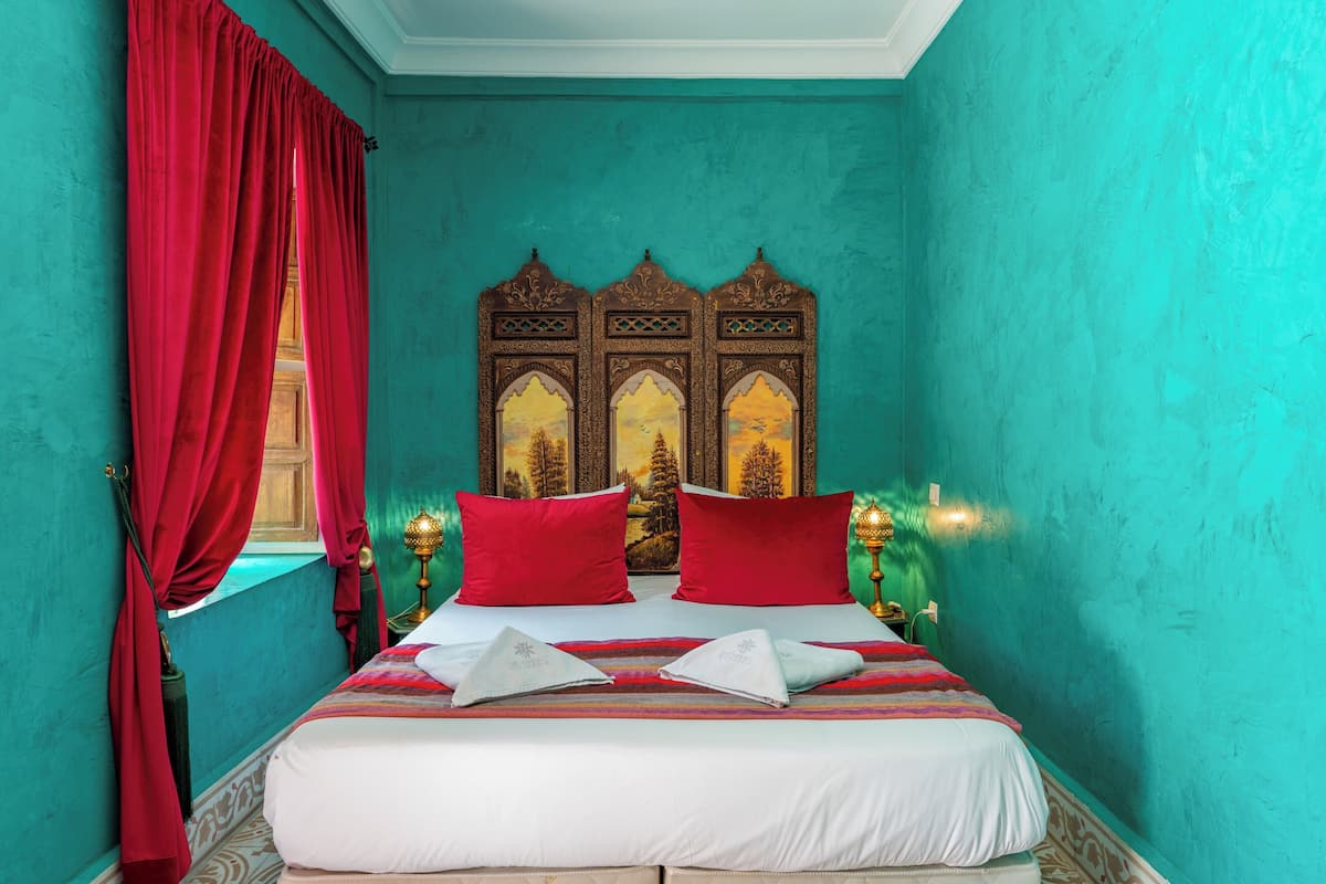 A bedroom with a bed, red curtains, a decorative headboard, and a window.