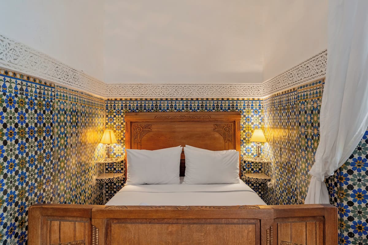 A neatly made bed with a wooden headboard, two bedside lamps, and a patterned tile wall.