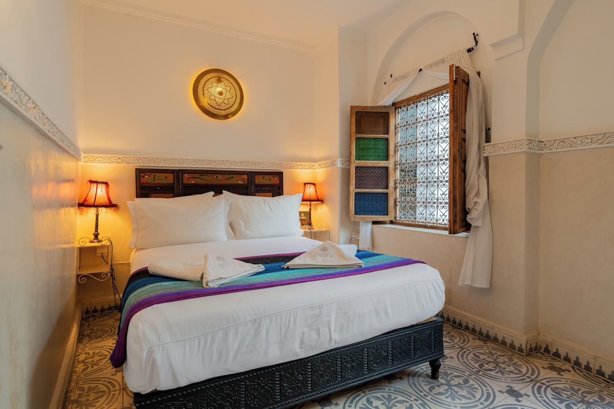 A neatly made bed with white linens, two bedside lamps, and a decorative wall hanging.