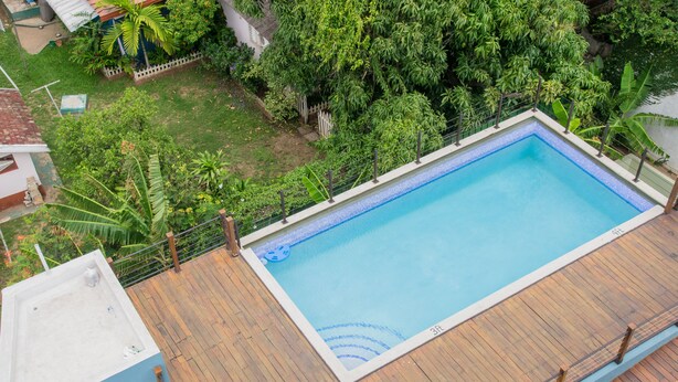 A rectangular swimming pool with a wooden deck surrounding it, set against a backdrop of lush greenery. - Brompton 40 by Pro Homes Jamaica (Kingston)