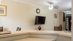 A living room with a flat-screen TV, a ceiling fan, a clock, and a vase on a white table. - Brompton 40 by Pro Homes Jamaica (Kingston)