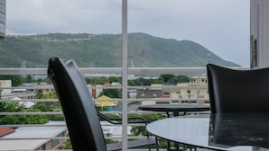 A balcony with a table and chairs, overlooking a cityscape with buildings and a mountain in the distance. - Brompton 40 by Pro Homes Jamaica (Kingston)