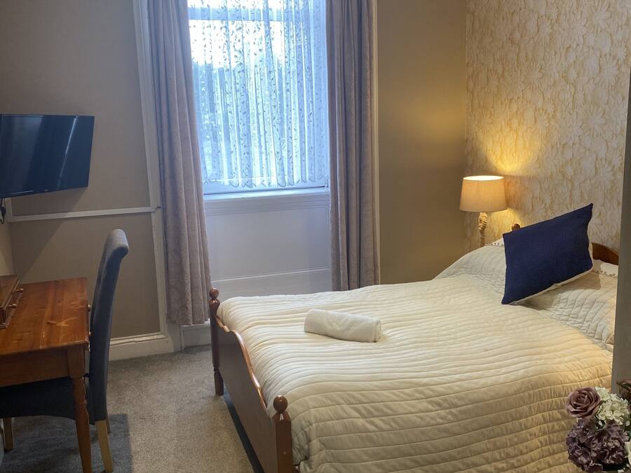A hotel room with a bed, a desk, a chair, a lamp, and a window with curtains.