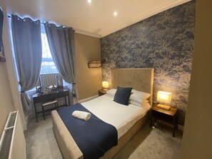Habitación de hotel con una cama grande, un escritorio, una silla, una lámpara y una ventana con cortinas.