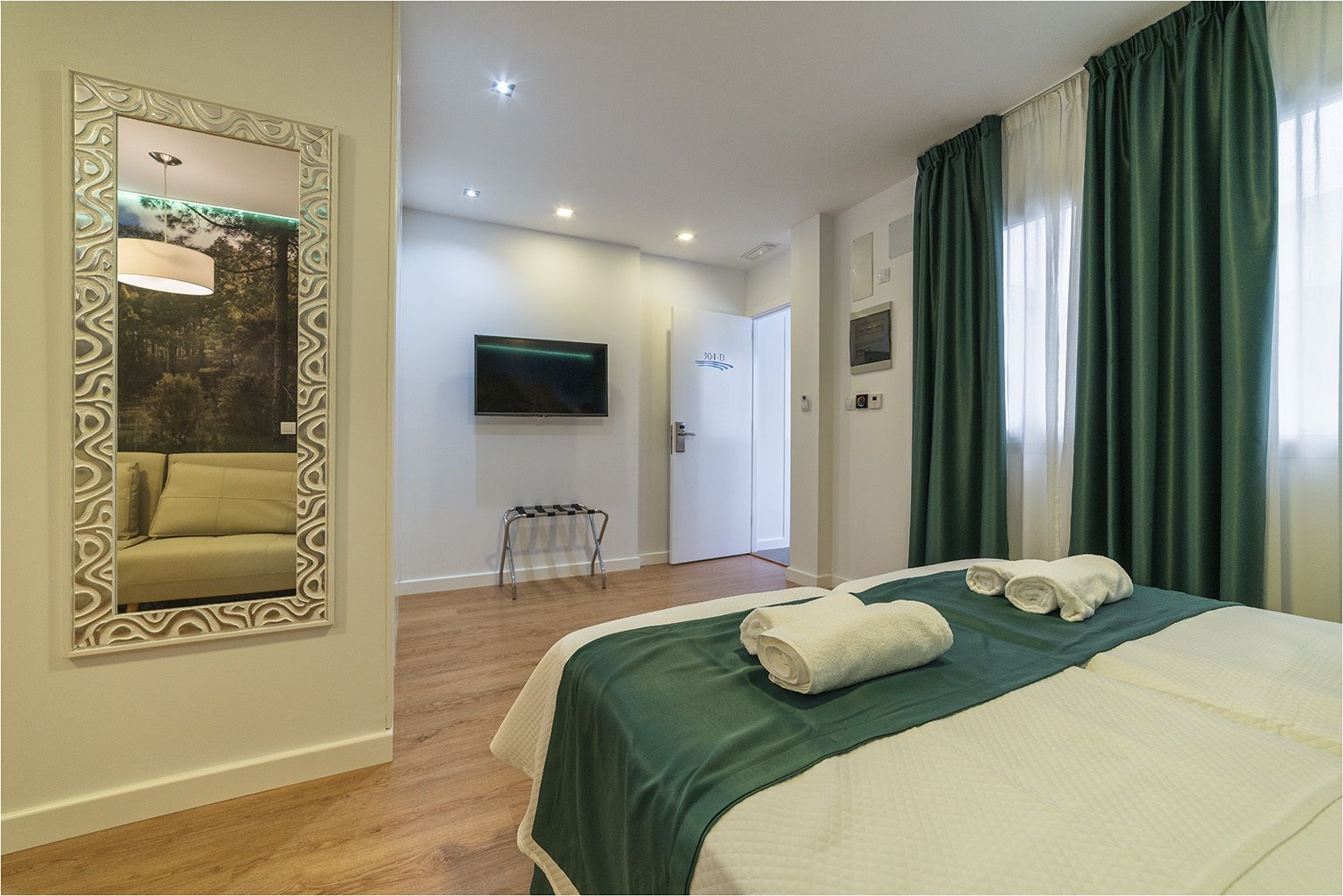 Habitació d'hotel amb un llit, televisió, mirall i una porta que dona a una altra habitació.