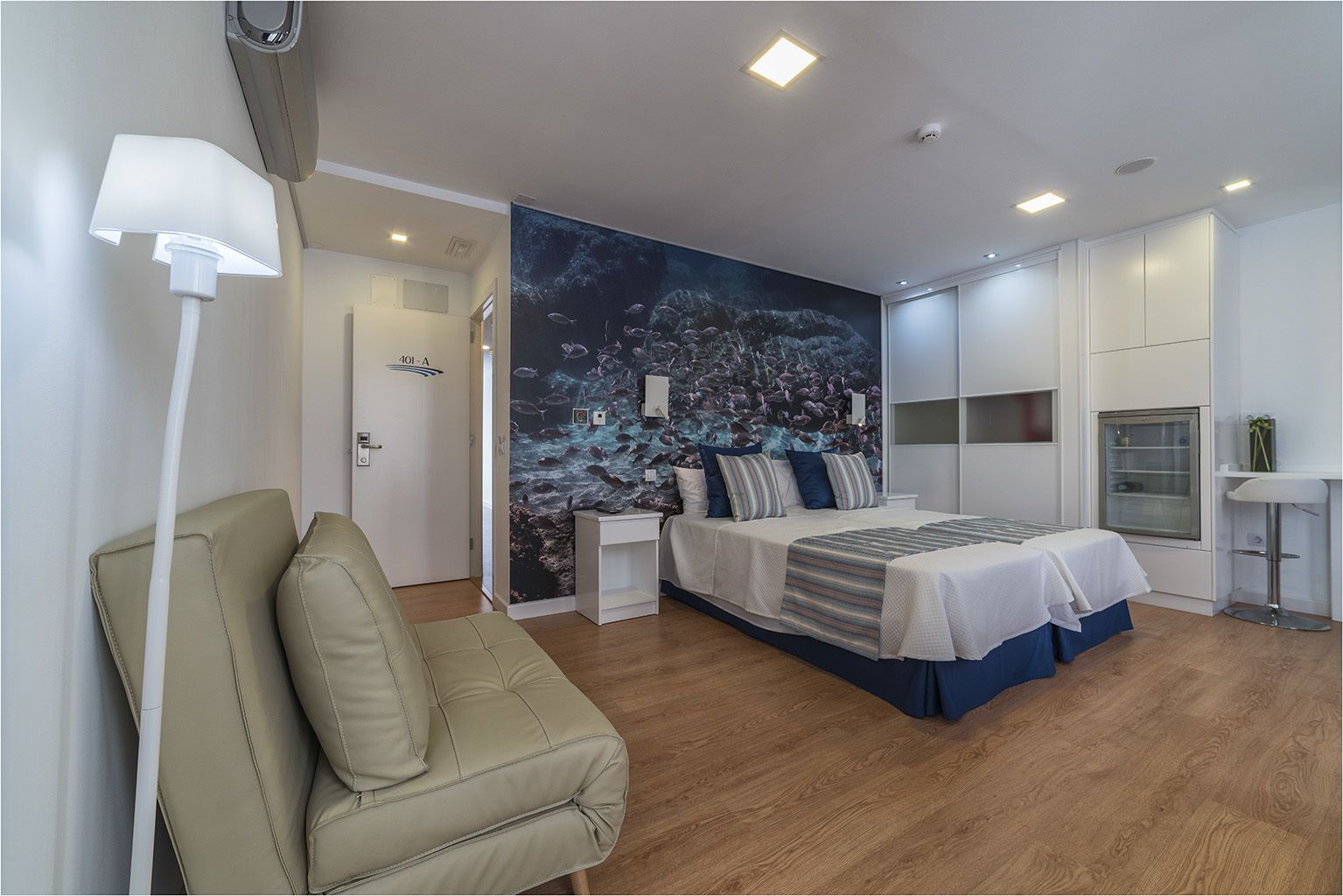 A modern bedroom with a bed, a seating area, a wall mural, and built-in storage.