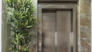 A modern elevator with a metallic finish, a large woven plant in a cylindrical pot, and stone-tiled walls. - Hotel Ciudad del Mar (Las Palmas de Gran Canaria)