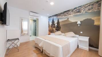 Ein Schlafzimmer mit einem großen Bett, einem an der Wand montierten Fernseher, einem Spiegel und einem Wandgemälde einer Berglandschaft.