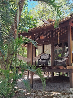 Un espacio de estar al aire libre techado, con mobiliario de mimbre y una pérgola de madera.