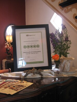 Un certificat d’excellence de TripAdvisor, encadré, est posé sur une table, à côté d’un vase de fleurs et de quelques brochures.