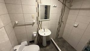 A bathroom with a toilet, sink, mirror, shower, and grab bars. - Hostal Anthony's (Lima)