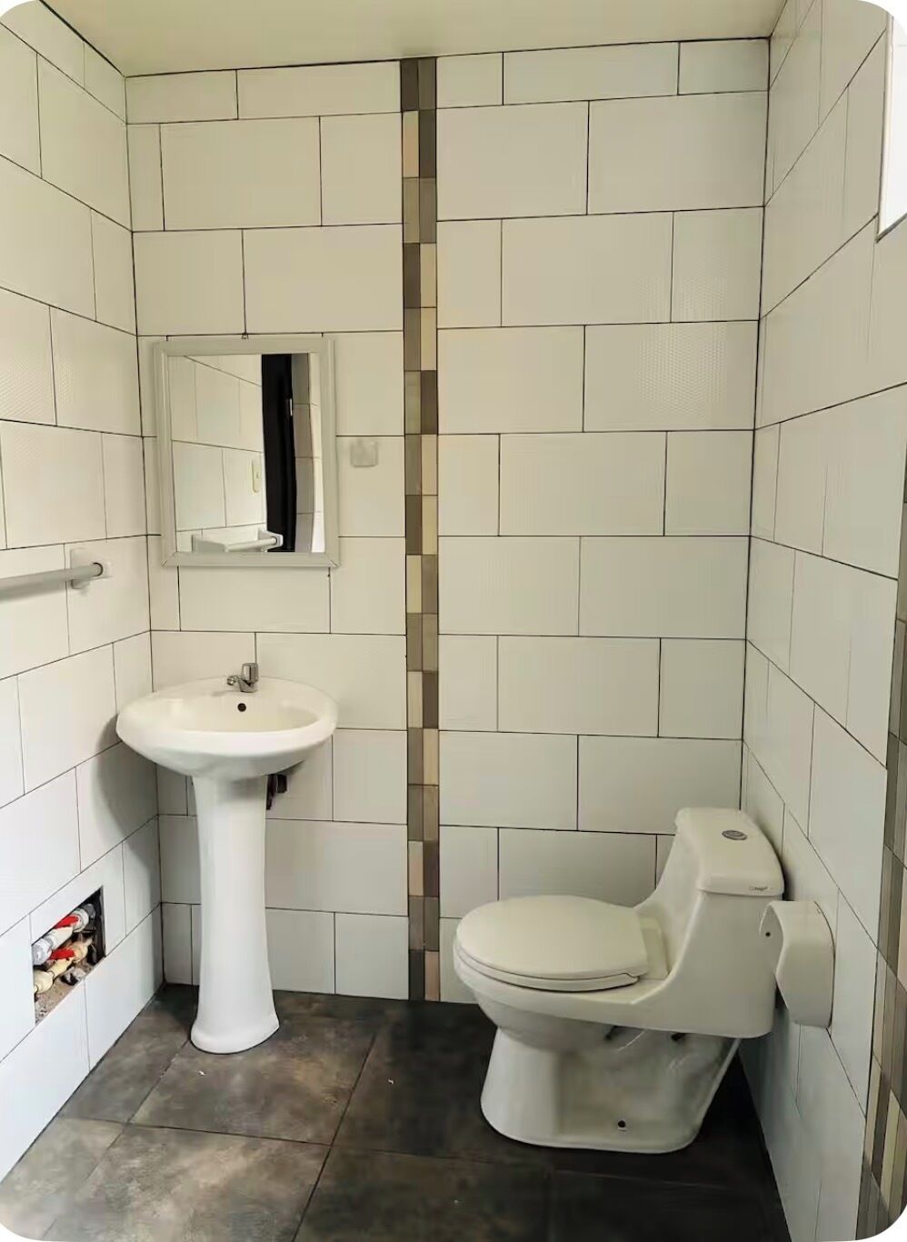 Un baño pequeño con azulejos blancos, un lavamanos pedestal, un inodoro y un espejo.