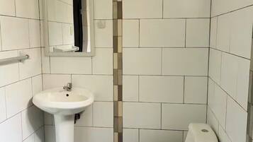 Un baño pequeño con azulejos blancos, un lavamanos pedestal, un inodoro y un espejo.