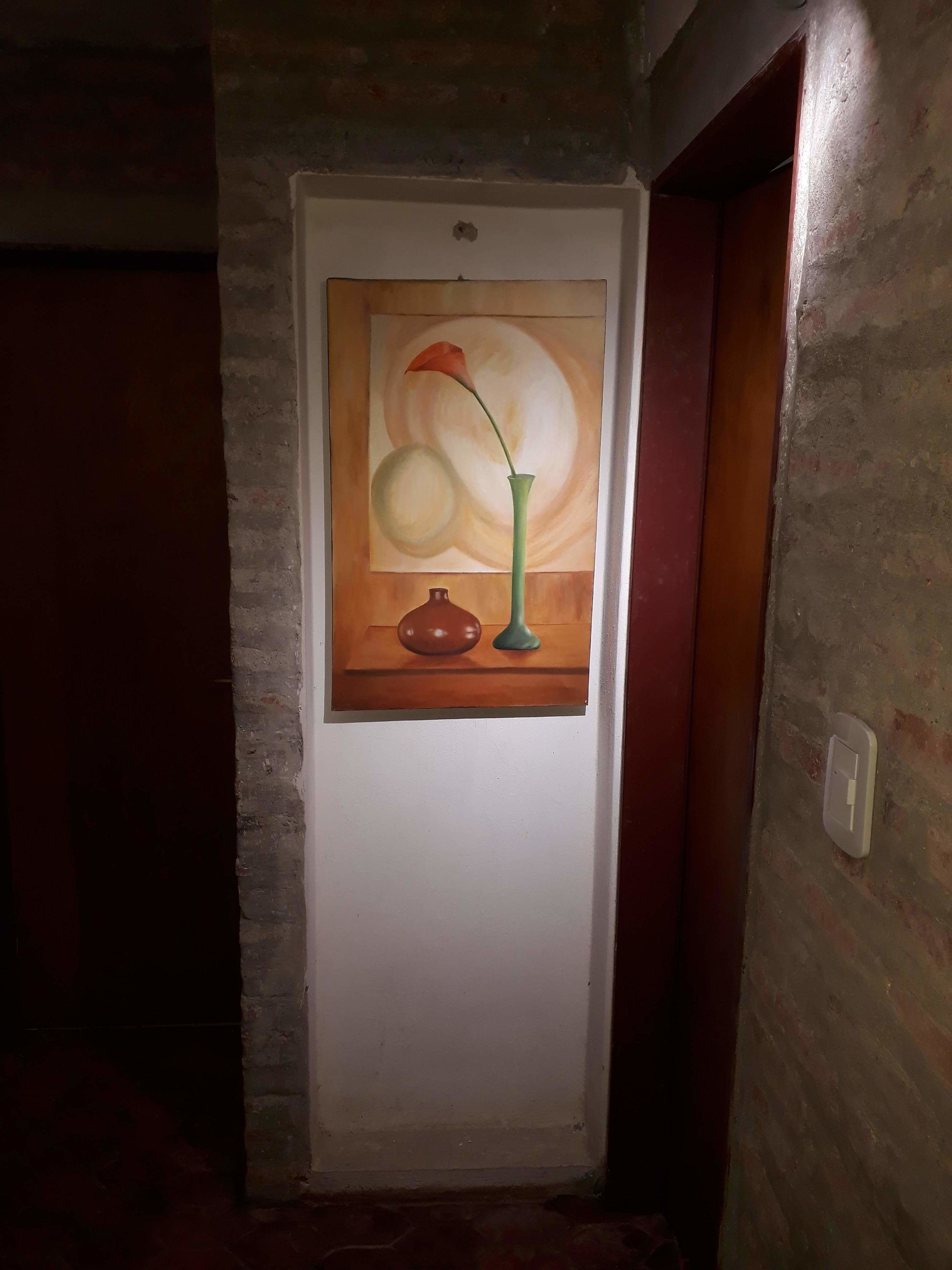 Un pasillo con una puerta que presenta un cuadro de un jarrón con una flor y fruta.