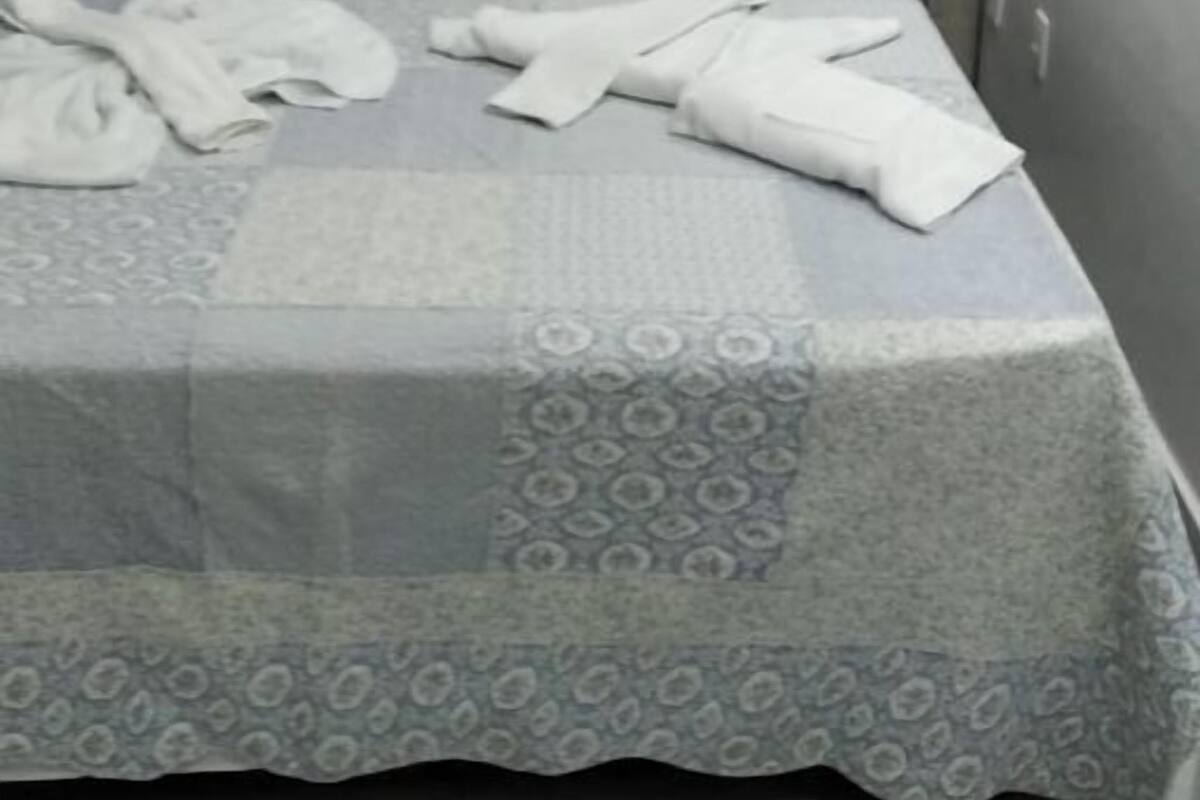 A hotel room with a bed, grey curtains, and an air conditioning unit.