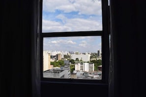 Vista desde una ventana con un paisaje urbano de fondo, que incluye varios edificios y un cielo despejado.