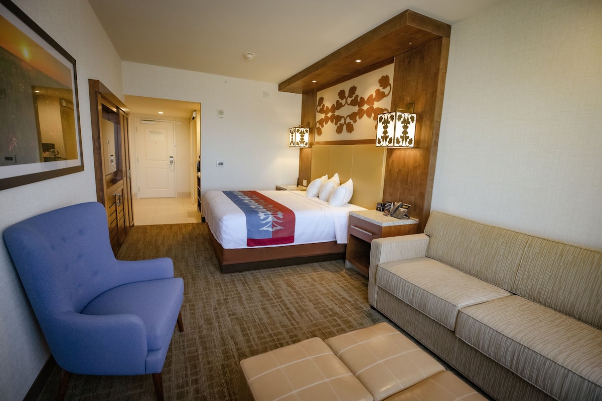 Ein Hotelzimmer mit einem Bett, einem blauen Sessel, einer Couch und einem kleinen Tisch mit einer Lampe.