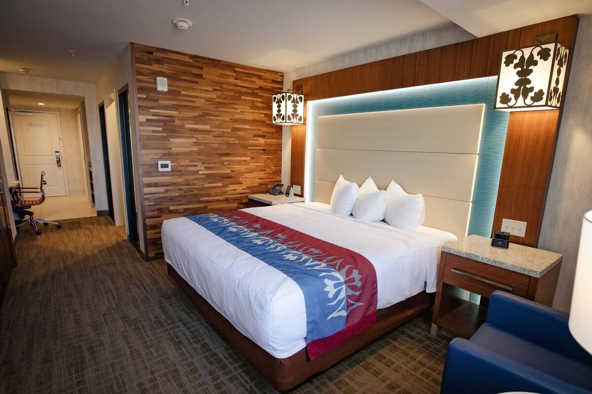 Ein Hotelzimmer mit einem großen Bett, Holzvertäfelung, einem Schreibtisch mit Lampe und einem Sessel.