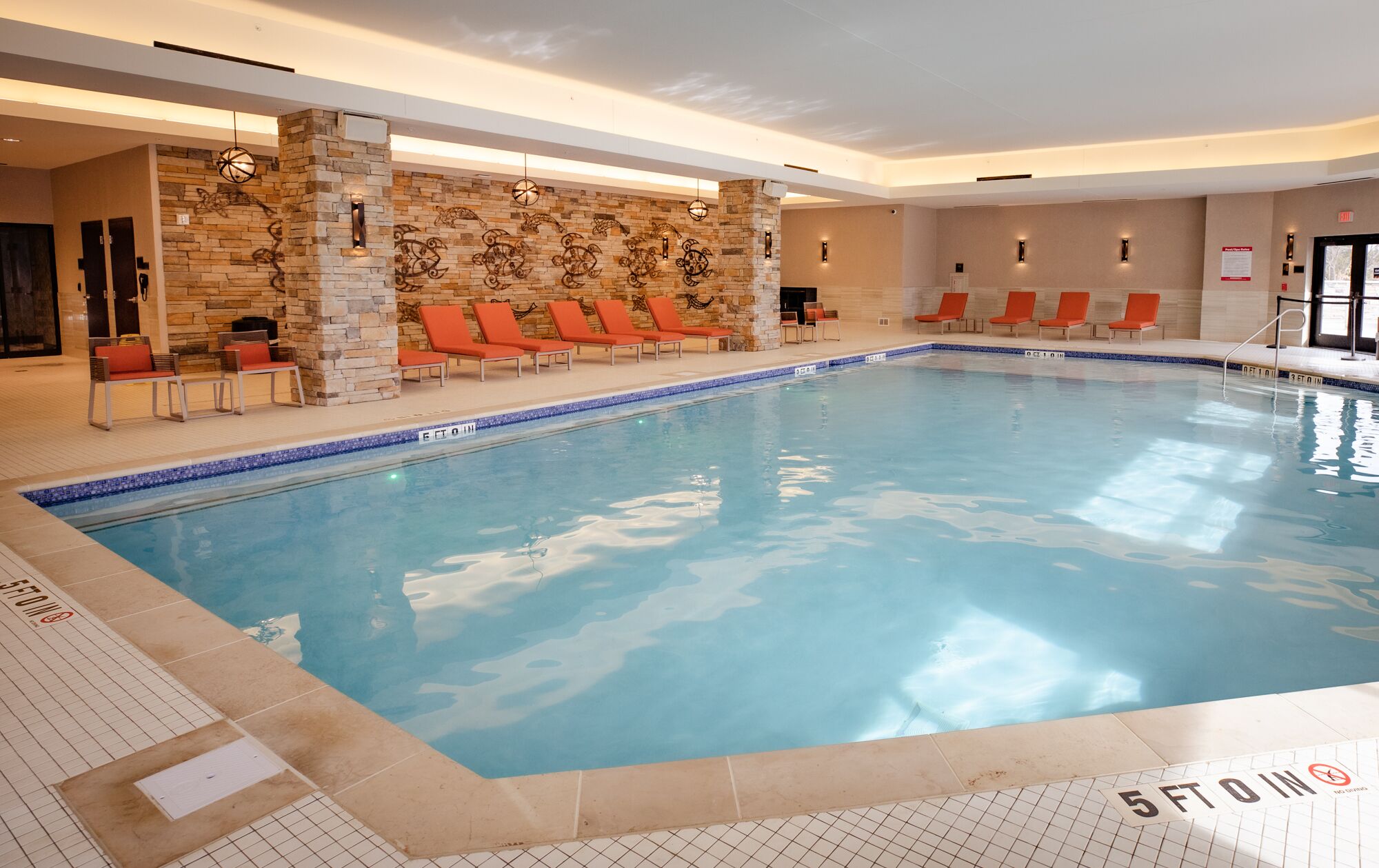 An indoor swimming pool with stone walls and red lounge chairs.