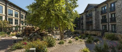 A courtyard with a central tree, stone pathways, and a pool area surrounded by buildings with balconies.