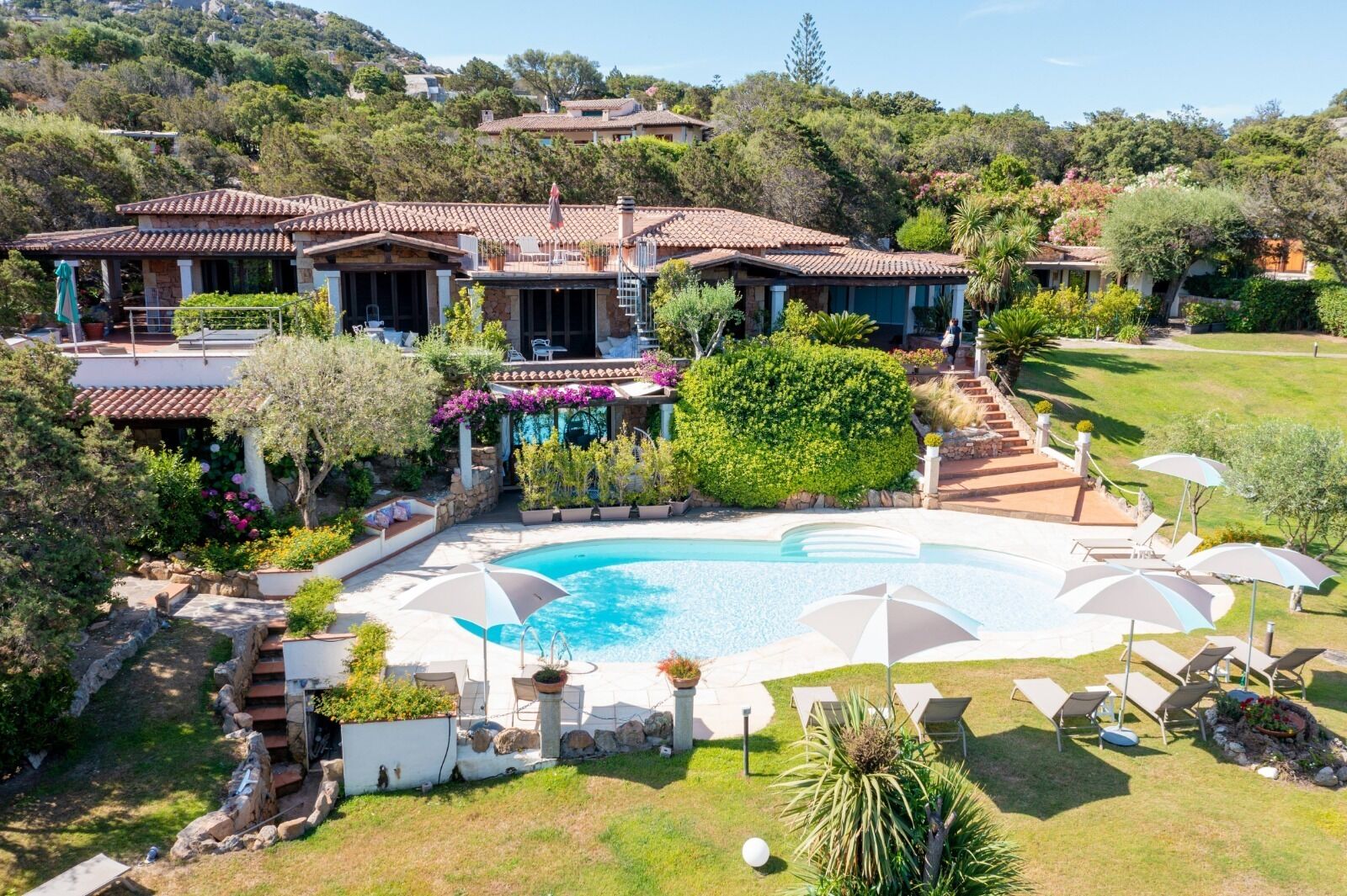 A large, private pool with lounge chairs and umbrellas, surrounded by lush greenery and a hillside backdrop.