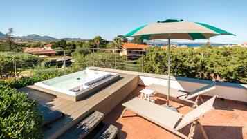 Una terraza en la azotea con un jacuzzi, mobiliario exterior y vistas del paisaje circundante.