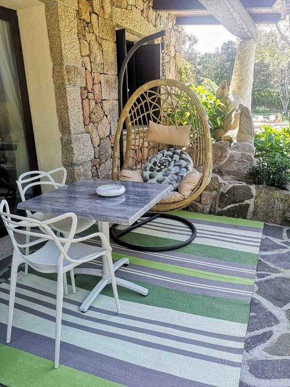 Un mur de pierres, une chaise en osier et une table avec des chaises blanches.