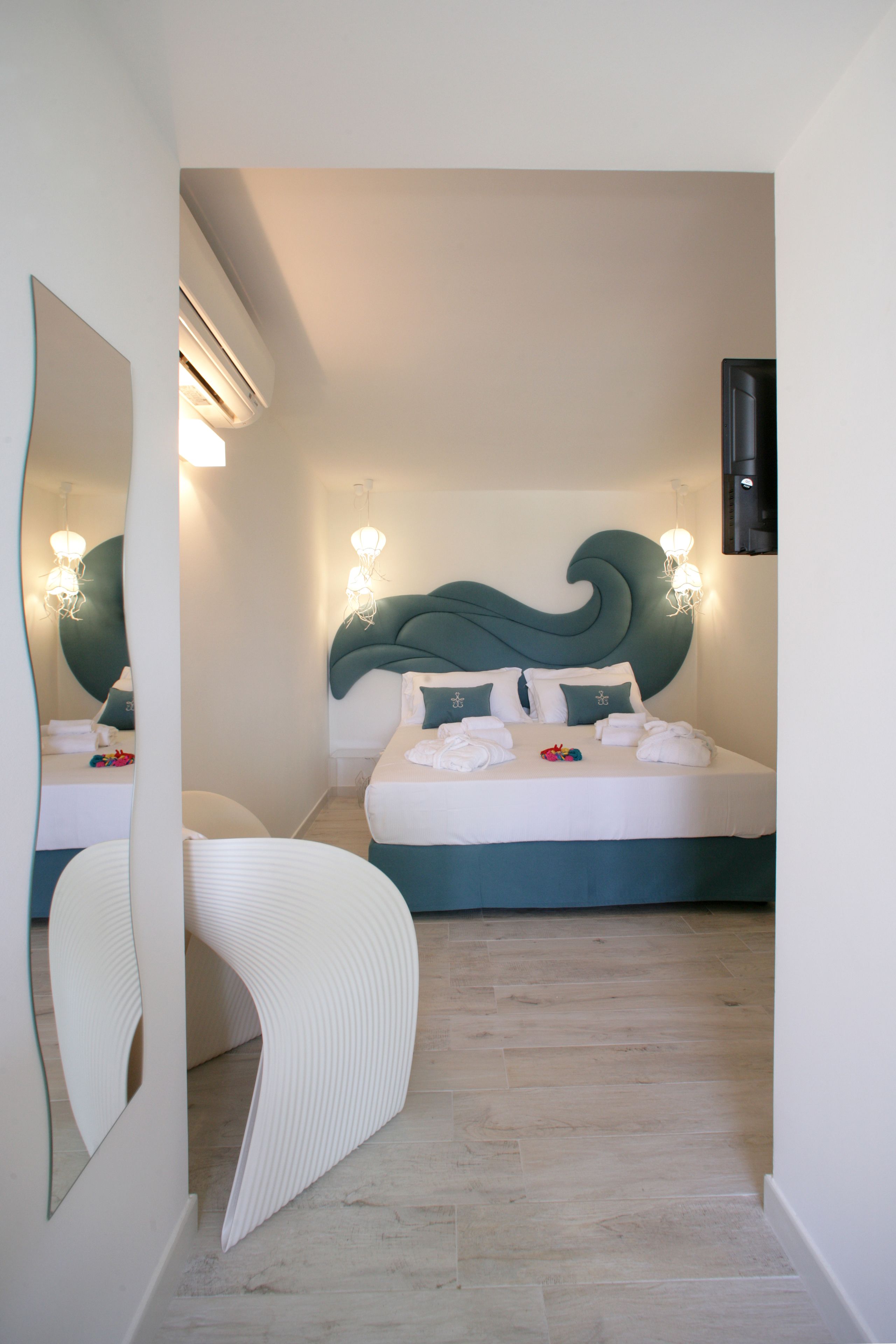 A modern bedroom with a curved headboard, a large mirror, and a bed with white linens and teal accents.