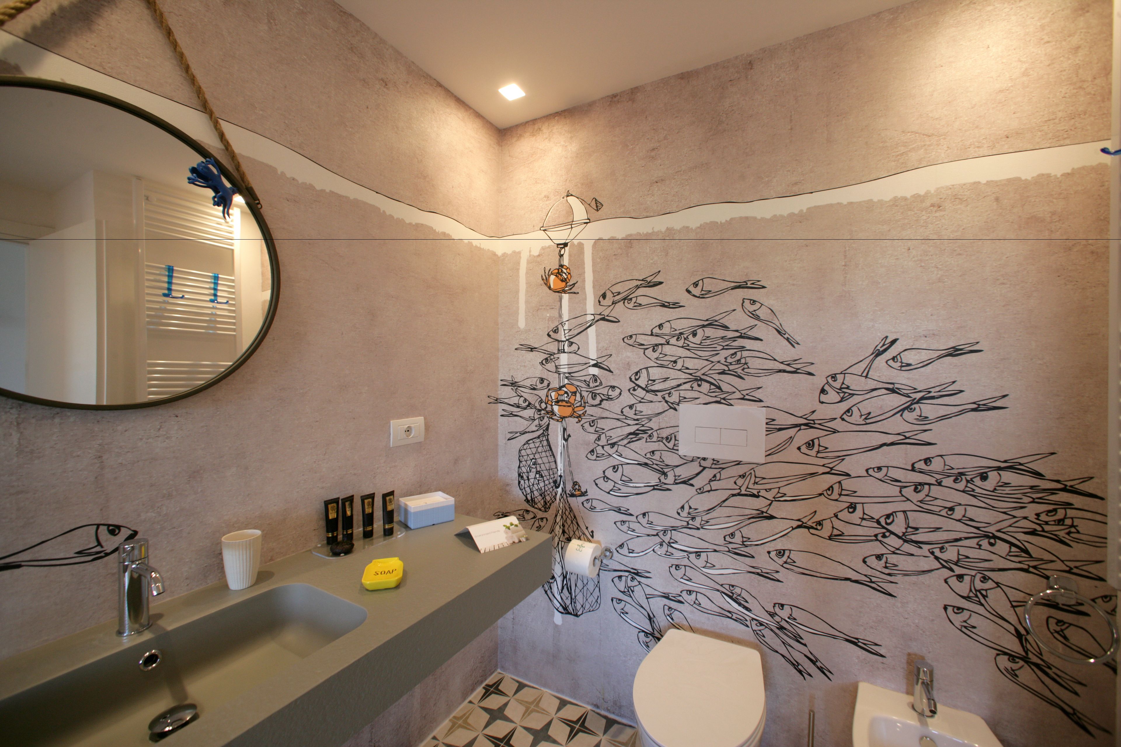 Un baño con un espejo grande, dos lavamanos, un inodoro y un mural de peces en la pared.
